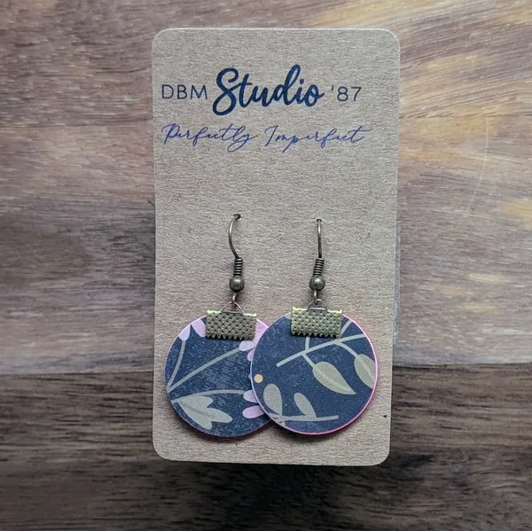 quarter size round earrings made from layers of paper modpodged together, Black with pink and green flowers and green with white polka dot back. The color of the sides made by the paper inside is pink. Bronze-tone findings.